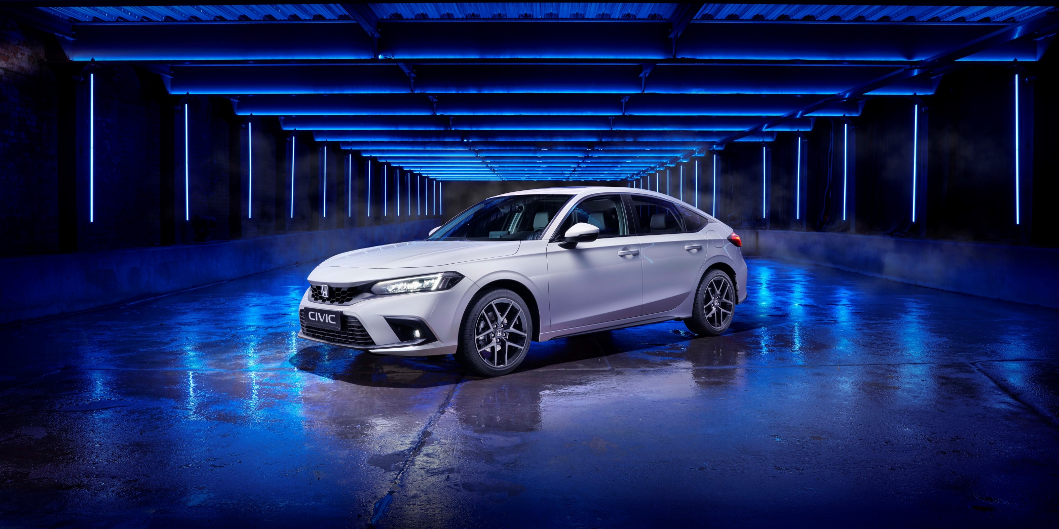 Skråvisning av en ny 2022 Honda Civic, med finish i hvitt og fotografert i et blåopplyst studio
